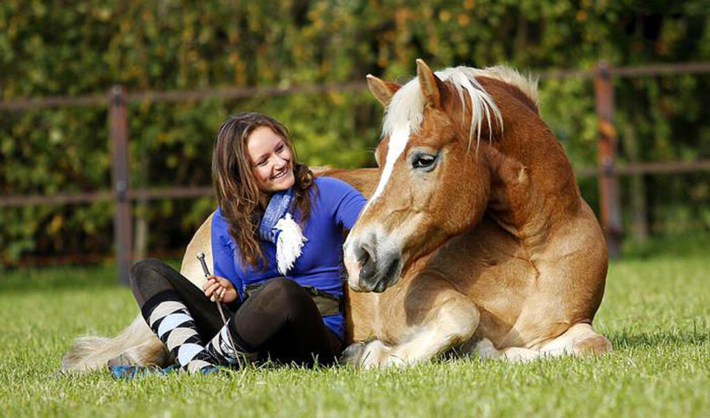 vrouw zittend naast een liggend paard